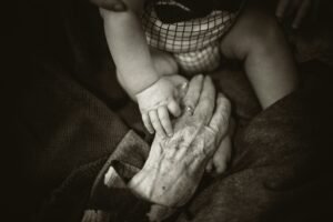 An elderly woman's hand gently holding a baby's hand, representing the importance of fall prevention and family caregiving