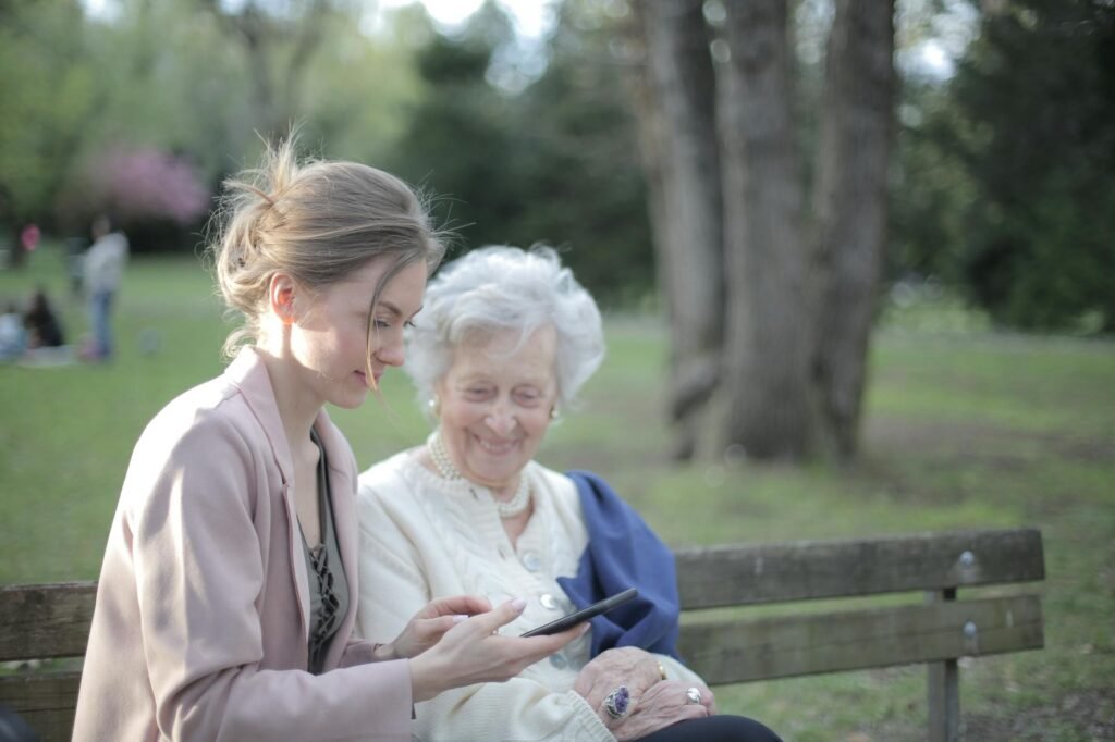 Adult daughter helping elderly mother use a smartphone outdoors