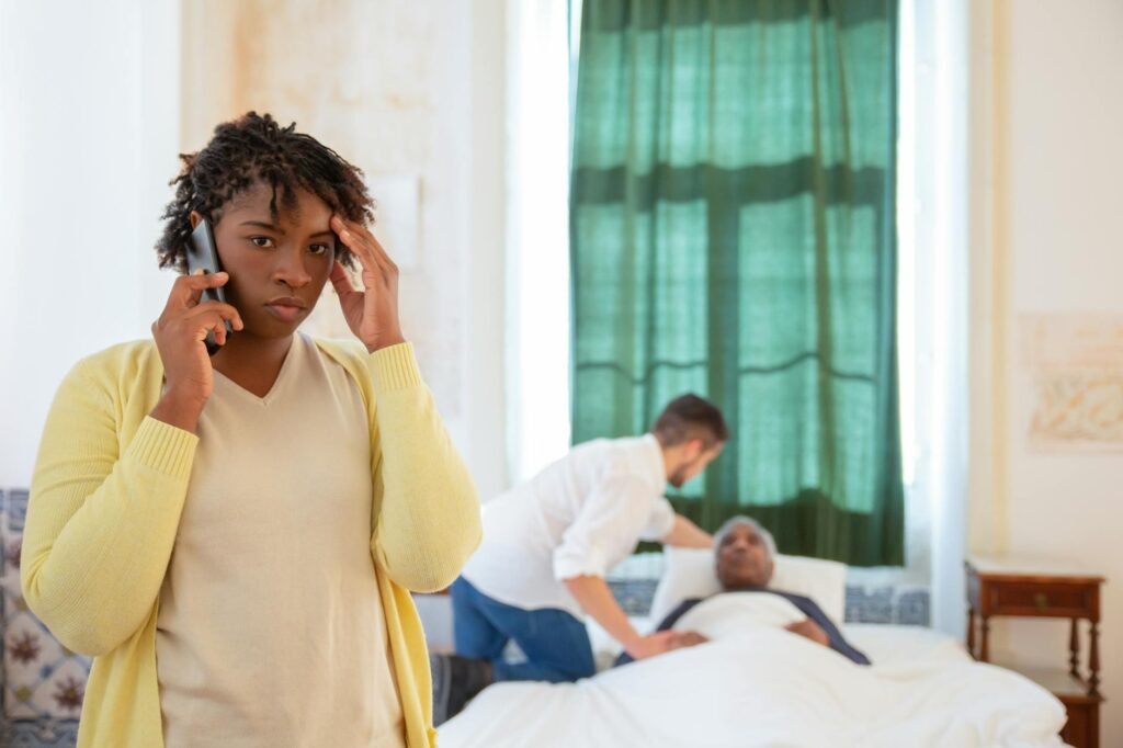 Worried family member on phone while caregiver assists elderly parent in hospital bed