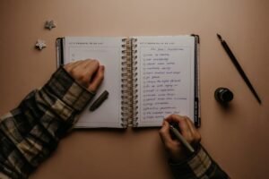 Hands writing in a notebook at a wooden desk — filling out an emergency information worksheet for family