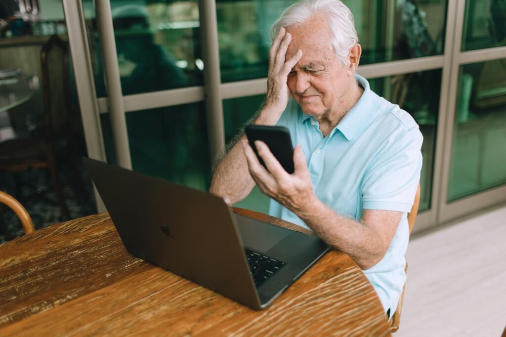 Elderly man frustrated by smartphone and laptop technology at home