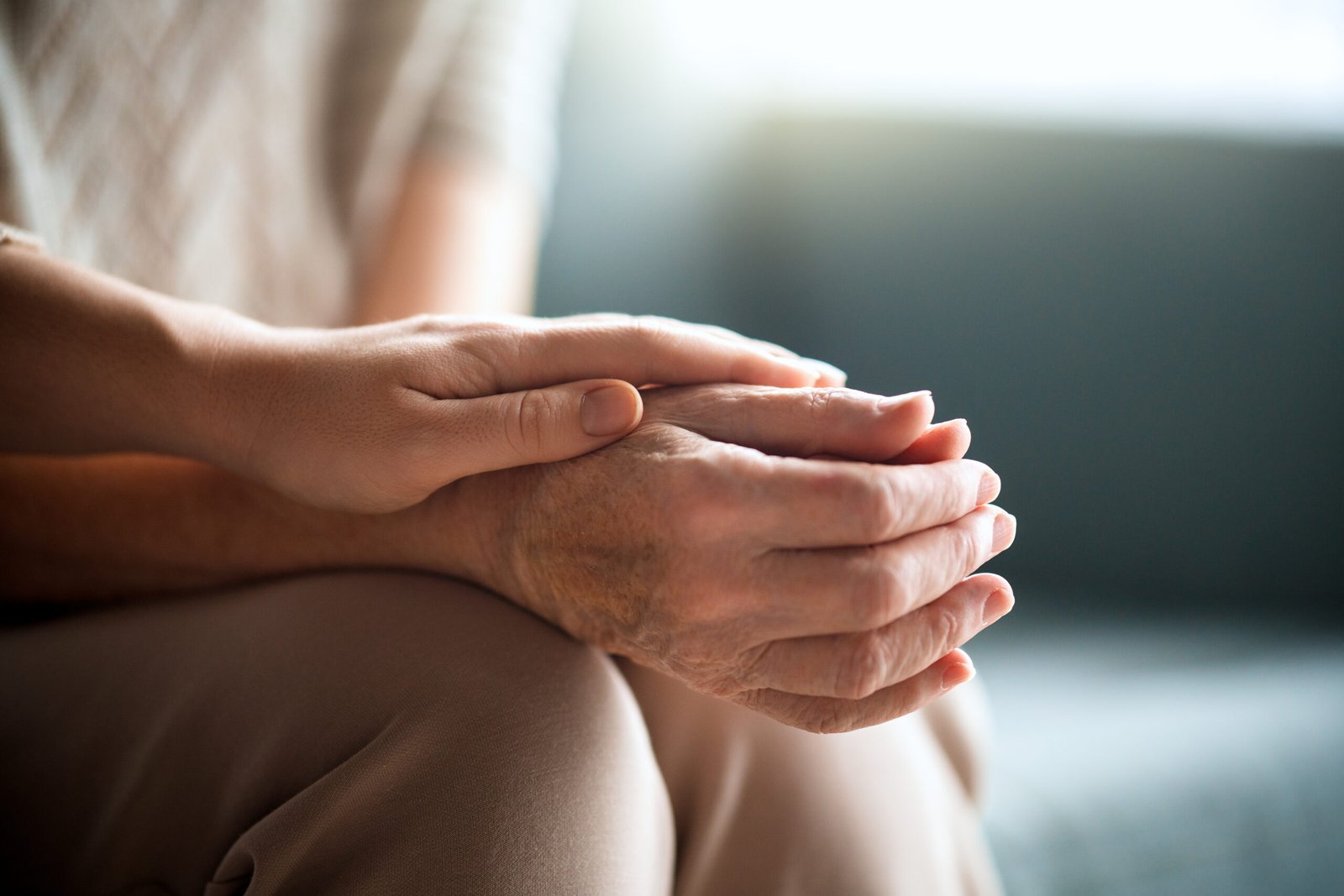 A younger hand resting gently on an older hand — quiet comfort at home